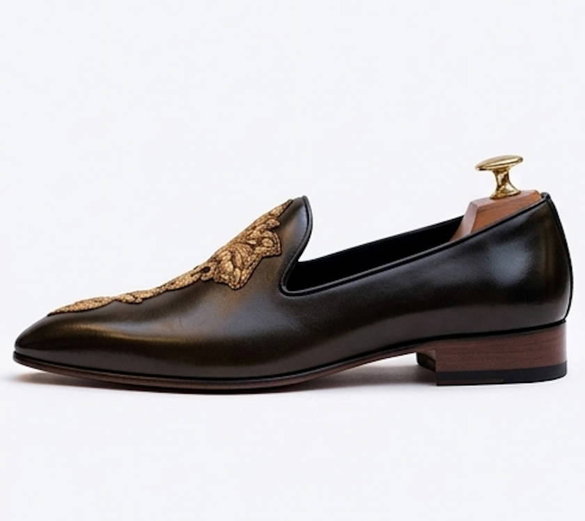 Pair of ornate black loafers with gold detailing on a beige background
