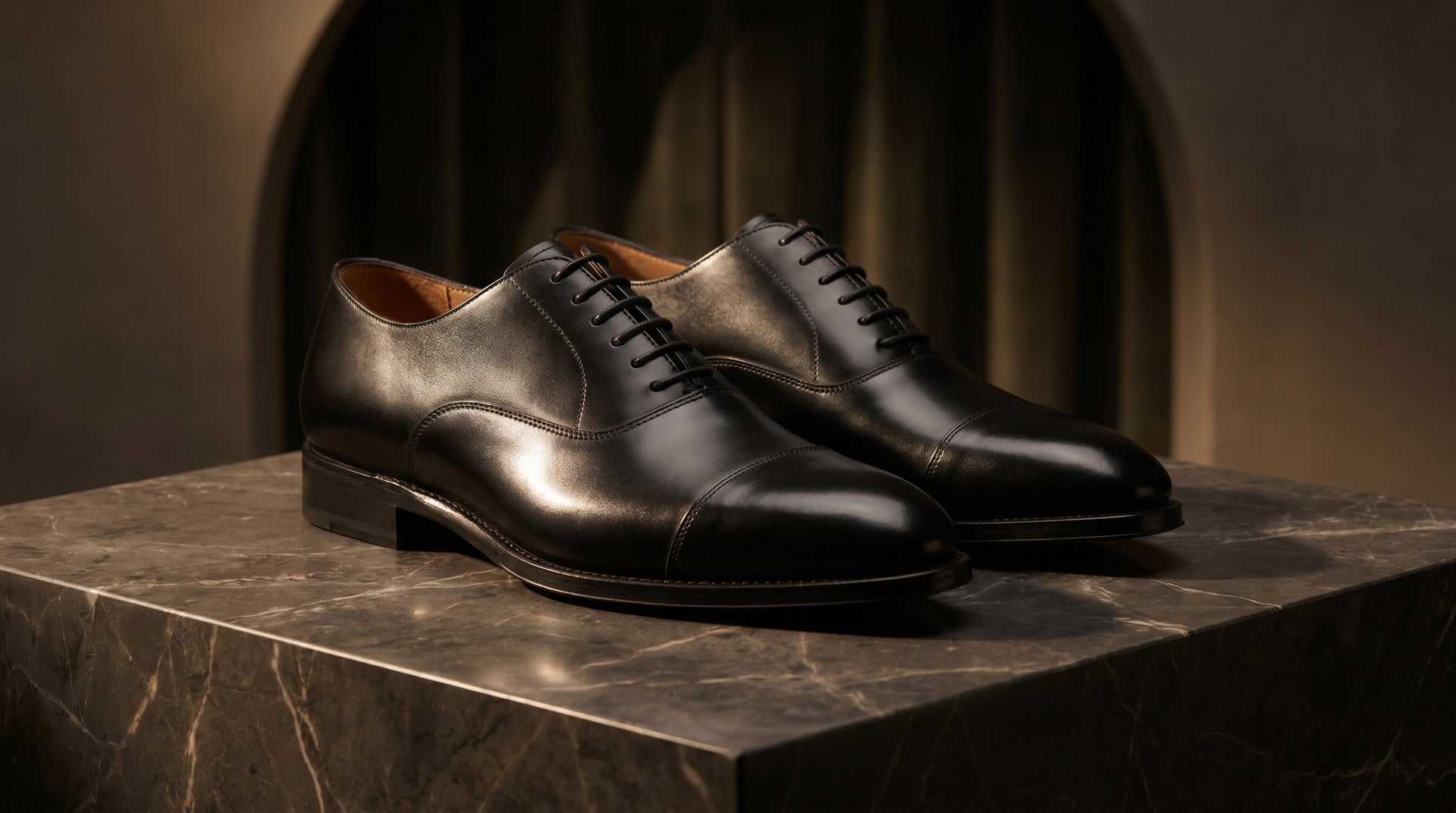 Pair of black dress shoes on a marble surface with a dark background